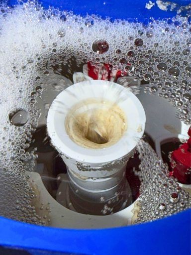 Weißer Abflussstopfen in schäumendem Wasser, umgeben von blauen und roten Teilen.